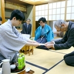 立会人の中田功八段（手前右）に封じ手を渡す藤井聡太王位（手前左）。中央奥は伊藤匠二冠＝２６日午後、徳島市、渭水苑