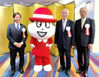 会社の７０周年記念式典で公式キャラクター「Ｑちゃん」と並ぶ副社長時代の塚本浩康社長（左端）と父の哲夫氏（中央）、当時３代目社長だった三宅宏和会長（いずれも六甲バター提供）