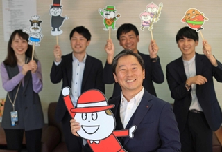ベビーチーズの公式キャラクターを手にし、社員に囲まれる塚本浩康社長（中央）＝神戸市中央区坂口通１、六甲バター（撮影・小林良多）
