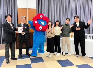 木下記念事業団の二星康親専務理事（左端）に入場券の目録を手渡す、三菱ＵＦＪ信託銀行の岡林茂伸大阪法人営業部長。大学生や万博キャラクターのミャクミャクも駆け付けた＝神戸市内（提供）