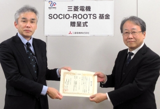 神戸市社会福祉協議会の玉田敏郎理事長（右）に贈呈書を手渡す三菱電機神戸製作所総務部の中島栄吉さん＝神戸市中央区磯上通３
