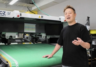 オンワード樫山との共同事業で使うイタリア社製裁断機の前で、今後の展望を語るロンタムの神農英道社長＝神戸市長田区川西通１