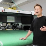 オンワード樫山との共同事業で使うイタリア社製裁断機の前で、今後の展望を語るロンタムの神農英道社長＝神戸市長田区川西通１