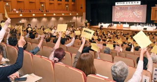 コープこうべ総代会で、採決時に議決書を掲げる総代たち＝神戸市中央区港島中町６、神戸ポートピアホテル