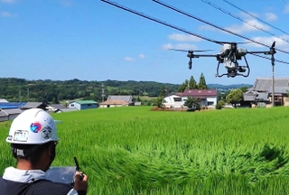 吉川町営農組合協議会の実証実験で水田上の電線を避けて飛行するドローン＝三木市吉川町金会（兵庫県提供）