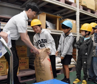 倉庫に入り、業務用の30キロ入り上白糖の重さを体感する子どもたち＝神戸市東灘区向洋町西５