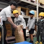 倉庫に入り、業務用の30キロ入り上白糖の重さを体感する子どもたち＝神戸市東灘区向洋町西５
