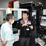最新モデルのレーザー加工機について来場者に説明する三菱電機の社員（中央）＝尼崎市長洲西通１、同社西日本メカトロソリューションセンター