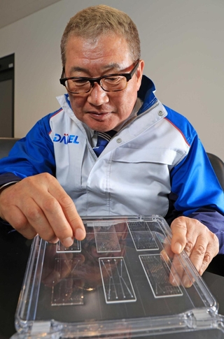 小さなガラス板に彫った溝に液体を入れ化学反応を起こす「マイクロプラント」について説明するダイセルの小河義美社長＝たつの市揖保川町馬場、同社播磨工場（撮影・小林良多）