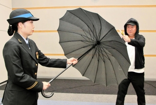 防刃傘を広げ、刃物を持った暴漢役と向き合う乗務員役の女性社員。傘の生地から相手が透けて見える＝１７日午後、大阪市北区、ＪＲ西日本本社