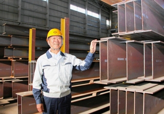 出荷を待つ主力製品のＨ形鋼。自慢の鋼材に触れる大和工業の小林幹生社長＝姫路市大津区勘兵衛町５
