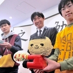 玩具のレゴでできた「ケンミン坊や」。灘中学・高校で、生徒たちから高村祐輝社長（中央）に渡された＝神戸市東灘区魚崎北町８