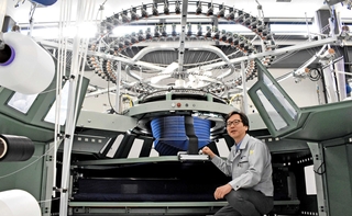 国内唯一の丸編み機メーカー、福原精機製作所の山田剛社長。円形の編み機にはあらゆる方向から糸が集まり、筒状の生地が出来上がる＝神戸市西区井吹台東町７