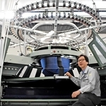 国内唯一の丸編み機メーカー、福原精機製作所の山田剛社長。円形の編み機にはあらゆる方向から糸が集まり、筒状の生地が出来上がる＝神戸市西区井吹台東町７