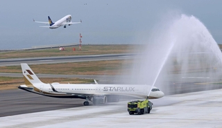 歓迎放水を受けて駐機場に入る台湾のスターラックス機。その奥でスカイマーク機が離陸した＝１８日午前、神戸市中央区、神戸空港（撮影・笠原次郎）