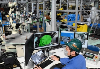 遠隔溶接システムを操作する高丸工業の高丸泰幸専務。実行ボタンをクリックすると左奥のロボットが動き出した＝西宮市朝凪町、同社