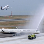 歓迎放水を受けて駐機場に入る台湾のスターラックス機。その奥でスカイマーク機が離陸した＝１８日午前、神戸市中央区、神戸空港（撮影・笠原次郎）