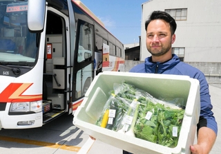 箱に詰めた野菜をバスに積み込む稲垣将幸さん＝神戸市西区白水３、神姫バス白水車庫