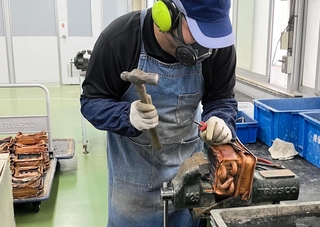 給湯器から銅製の熱交換器を取り出し、さらに分解する作業者（ノーリツ提供）
