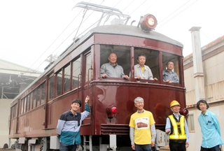 正面と側面の片方が復元された「デ１０１」とまもり隊のメンバーら＝神戸市北区鈴蘭台南町９、神戸電鉄鈴蘭台車庫