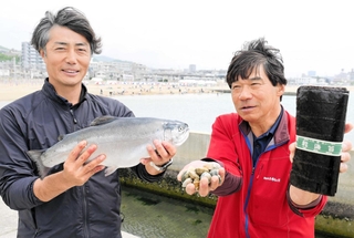 手がけるノリやアサリ、サーモンを持つすまうら水産の森本明会長（右）と若林良代表＝神戸市須磨区須磨浦通６