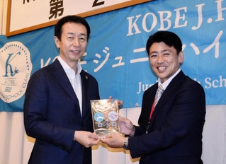 ＫＯＢＥジュニアハイスクールクラブの岩田哲也理事長（右）から、オフィシャルパートナーの楯を受け取るホームドライの太白守治社長＝神戸市中央区