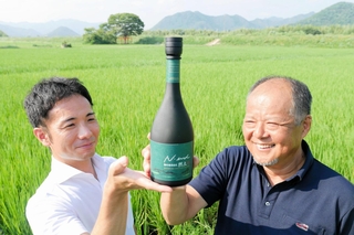 原料の酒米・山田錦の田を背に、日本酒「然土」を手にする藤原久和さん（右）と宝酒造の新宅恒基さん＝西脇市蒲江