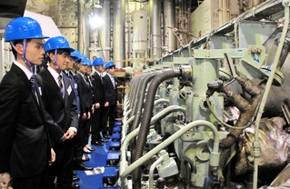 ヘルメット姿で「ルミナス神戸２」のエンジンルームを見学するジャパンエンジンコーポレーションの内定者ら＝神戸港中突堤