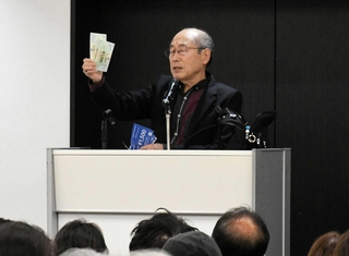 株主優待券を手に講演する桐谷広人さん＝神戸国際会館
