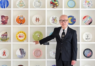 フェリシモ本社の商談スペースの一角に飾られたチャリティープレートの前に立つ矢崎和彦社長。プレートは同社の特色の一つの基金付き商品で、国連教育科学文化機関（ユネスコ）と約３０年にわたり共同実施する＝神戸市中央区新港町（撮影・大田将之）