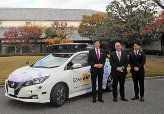 自動運転で経由する白鶴酒造資料館（奥）の前で、使用車両と記念撮影する久元喜造・神戸市長（左端）ら＝神戸市東灘区住吉南町４