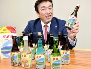 「地球の歩き方」デザインのフィルムを包装した日本酒を手にする日本テクノロジーソリューションの岡田耕治社長＝神戸市中央区港島南町７