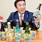 「地球の歩き方」デザインのフィルムを包装した日本酒を手にする日本テクノロジーソリューションの岡田耕治社長＝神戸市中央区港島南町７