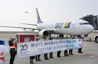 神戸空港の開港20年を祝う横断幕を広げ、搭乗客を見送る空港関係者ら＝20日午前、同空港（撮影・大田将之）