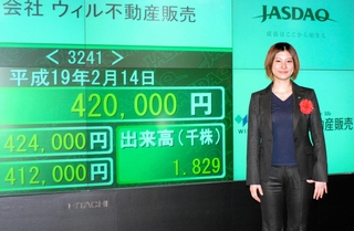 念願だったジャスダック市場への株式上場を果たし、株価モニターの前に立つ友野泉さん＝２００７年２月（ウィル提供）