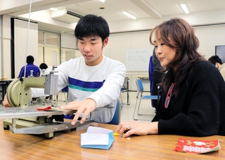インプルーヴ代表の鈴木弘美さん（右）に見守られながら、専用の機械でリンキングを行う生徒＝神戸市灘区岩屋北町６、青陽灘高等支援学校