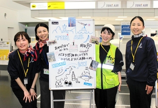 就航１年を記念した手書きのホワイトボードで乗客を迎えたトキエアのスタッフ＝神戸空港