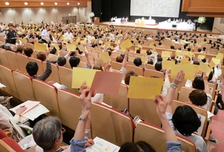 議案の採決時に議決票を挙げるコープこうべの総代ら＝神戸市中央区港島中町６