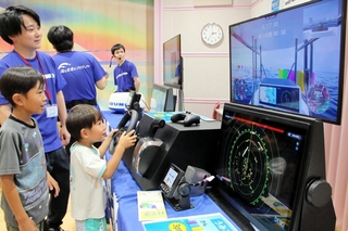古野電気のブースで、船の操縦を疑似体験する子どもら＝西宮市北口町