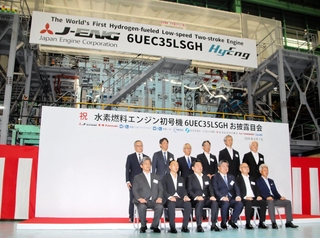 完成した水素エンジンの前で記念撮影する、ジャパンエンジンコーポレーションや川崎重工業の関係者＝明石市二見町南二見、ジャパンエンジンコーポレーション
