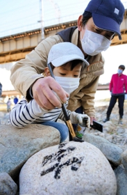 積み上げた石に追悼の思いなどをしたためる親子＝宝塚市の武庫川中州