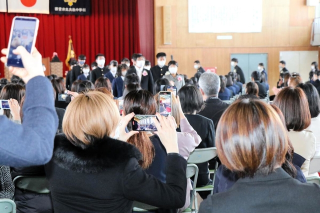 卒業式会場を後にする生徒を収めようとスマートフォンを構える保護者ら＝西宮市神原、大社中学校