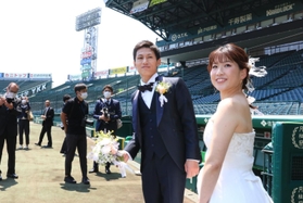 撮影のためグラウンドに入り笑顔の新郎新婦＝２３日、西宮市甲子園町、阪神甲子園球場