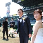 撮影のためグラウンドに入り笑顔の新郎新婦＝２３日、西宮市甲子園町、阪神甲子園球場