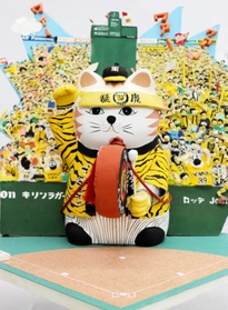 甲子園球場で、ジェット風船を飛ばすファンを背景に太鼓をたたくネコをデザインした貯金箱＝尼崎市西本町北通３