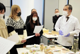 音羽ＤＥＬＩの担当者らから新メニューの試作品について説明を受ける武庫川女子大学の学生ら＝西宮市池開町（武庫川女子大学提供）
