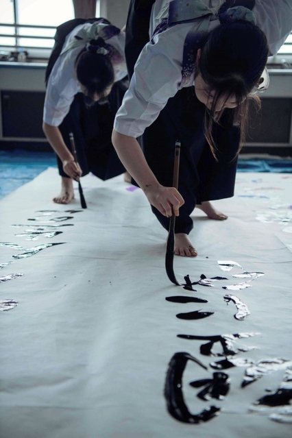 太筆を握り、躍動感あふれる動きで書をしたためていく高校生（ブランドブックより）