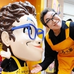 得意の変顔をかたどったマスコット人形と並ぶコロッケさん＝尼崎市七松町１