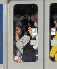 脱線事故現場前を通過する電車内で手を合わせる女性ら＝尼崎市久々知