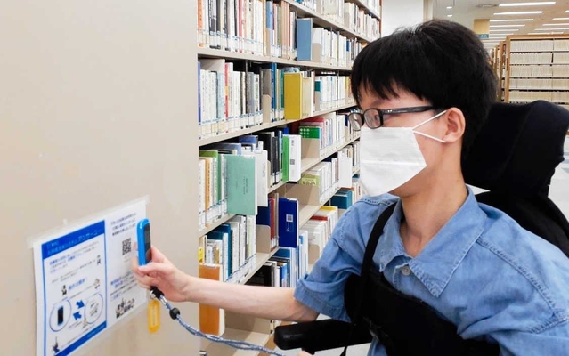 専用端末でＱＲコードを読み取り、介助支援を依頼する車いす利用者＝関西学院大学西宮上ケ原キャンパス図書館